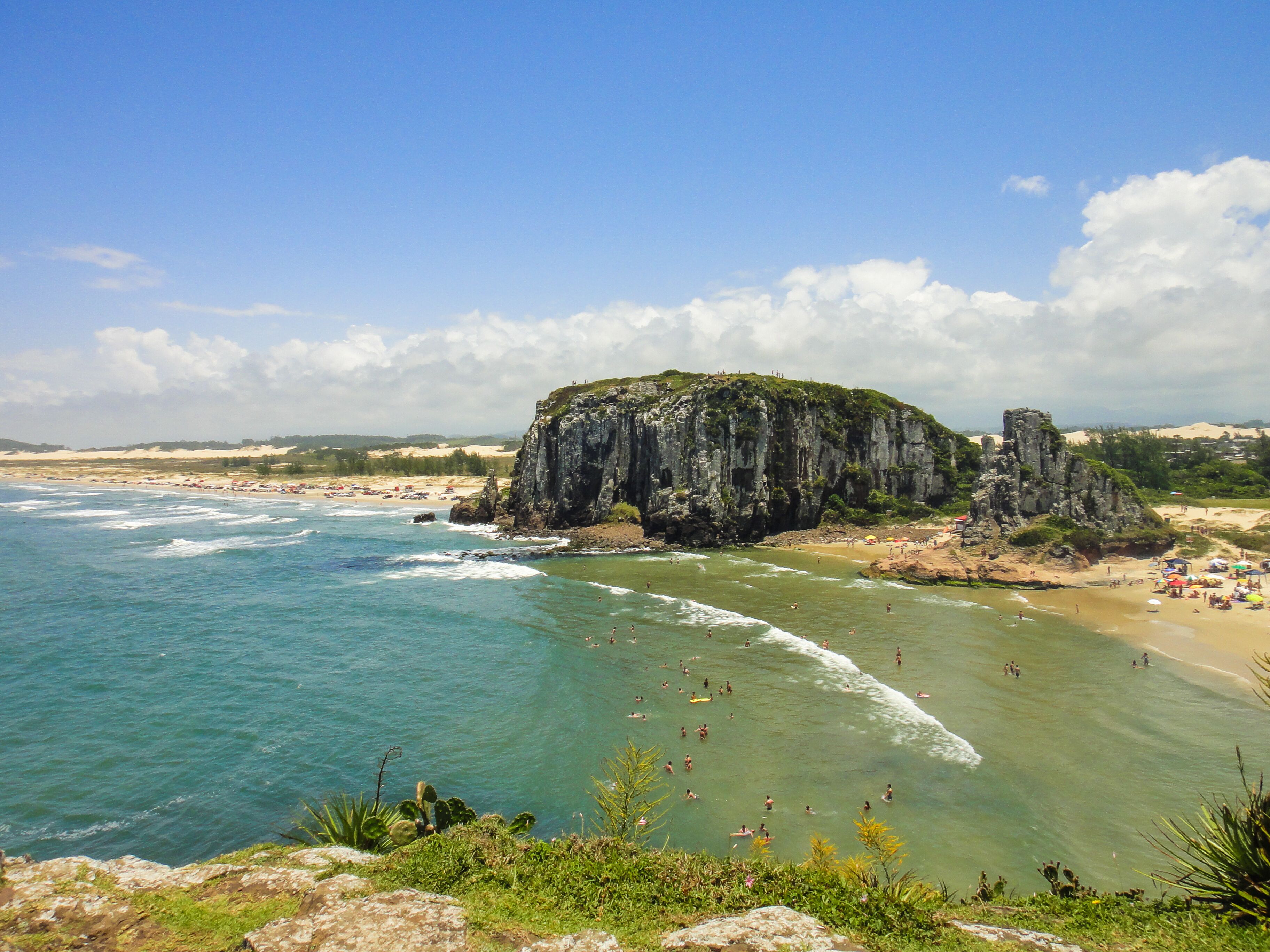Paisagem costeira com um penhasco imponente, praias de areia e águas azul-claras.