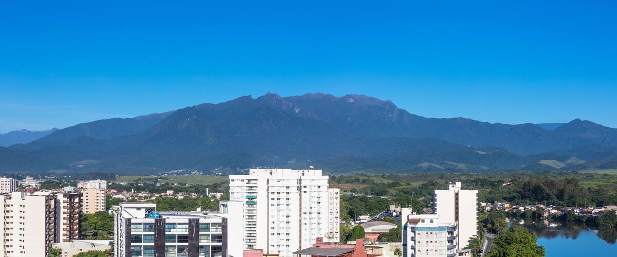 A cityscape with modern buildings, a lake, and a mountain range in the background.