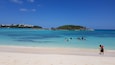 Una spiaggia con acque turchesi cristalline, una riva sabbiosa e una piccola isola con terreno roccioso sullo sfondo.