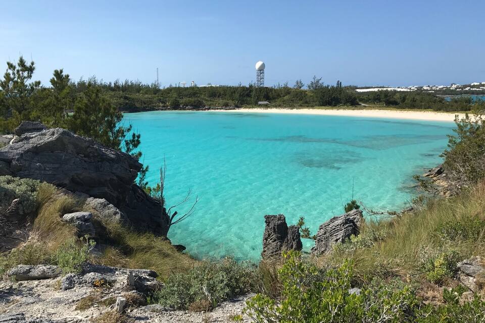 Et kystlandskab med krystalklart turkis vand, klippeformationer og en sandstrand.