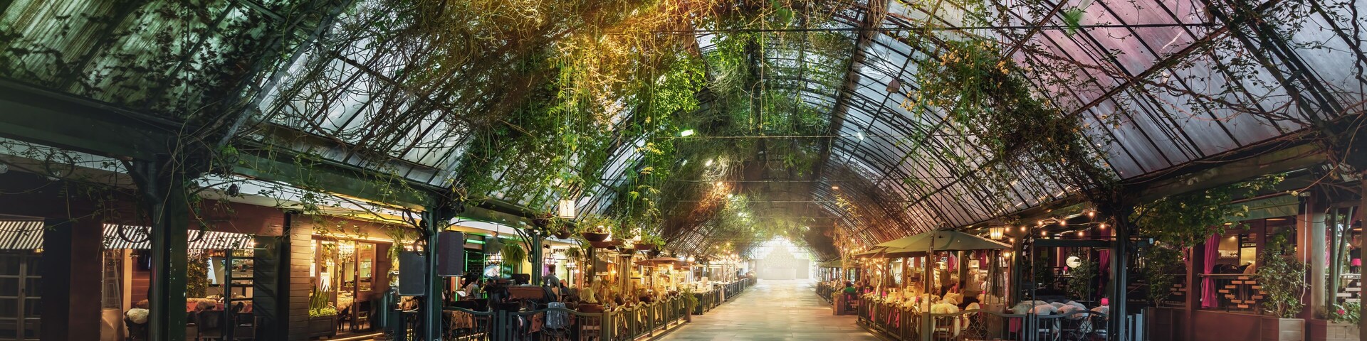 Un mercado interior con techo de cristal, plantas y varios puestos.