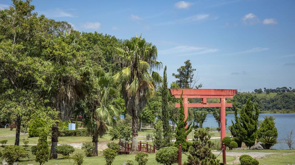 A park with a red torii gate, lush greenery, and a lake.