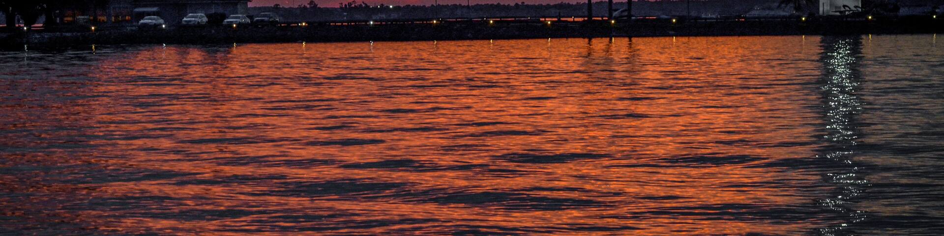 A sunset over a body of water with a lighthouse and palm trees.