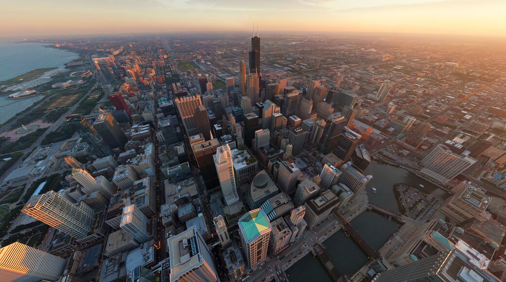 Aerial view of a sprawling cityscape, where the iconic Willis Tower pierces the skyline amidst the warm glow of the setting sun, Chicago, Illinois, United States.