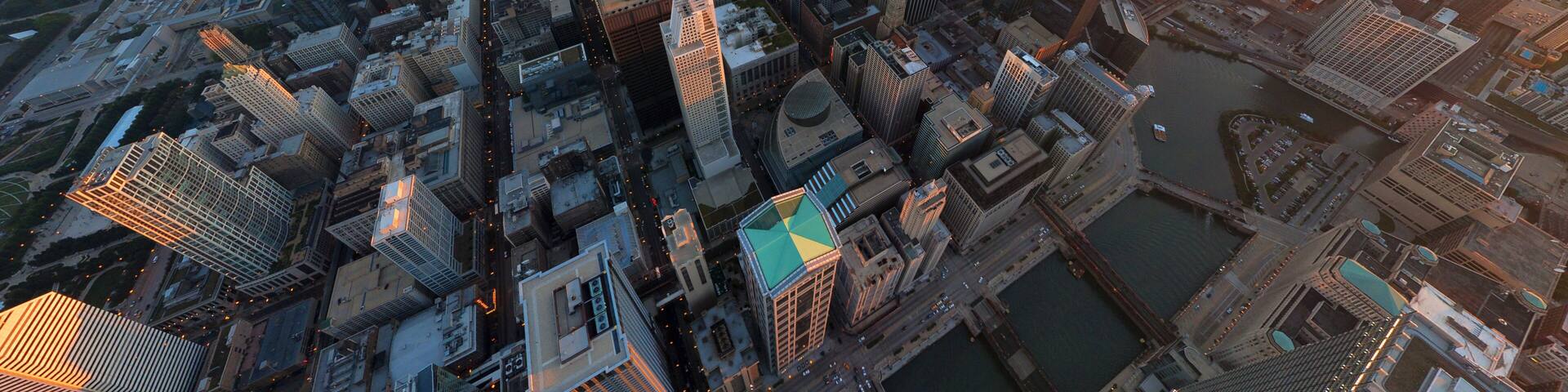 Aerial view of a sprawling cityscape, where the iconic Willis Tower pierces the skyline amidst the warm glow of the setting sun, Chicago, Illinois, United States.
