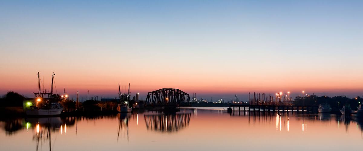 A calm harbor at dusk with a bridge and boats.