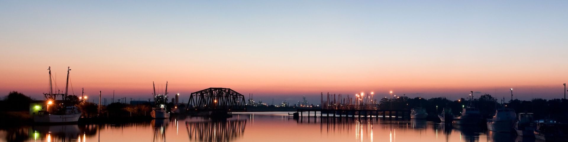 A calm harbor at dusk with a bridge and boats.