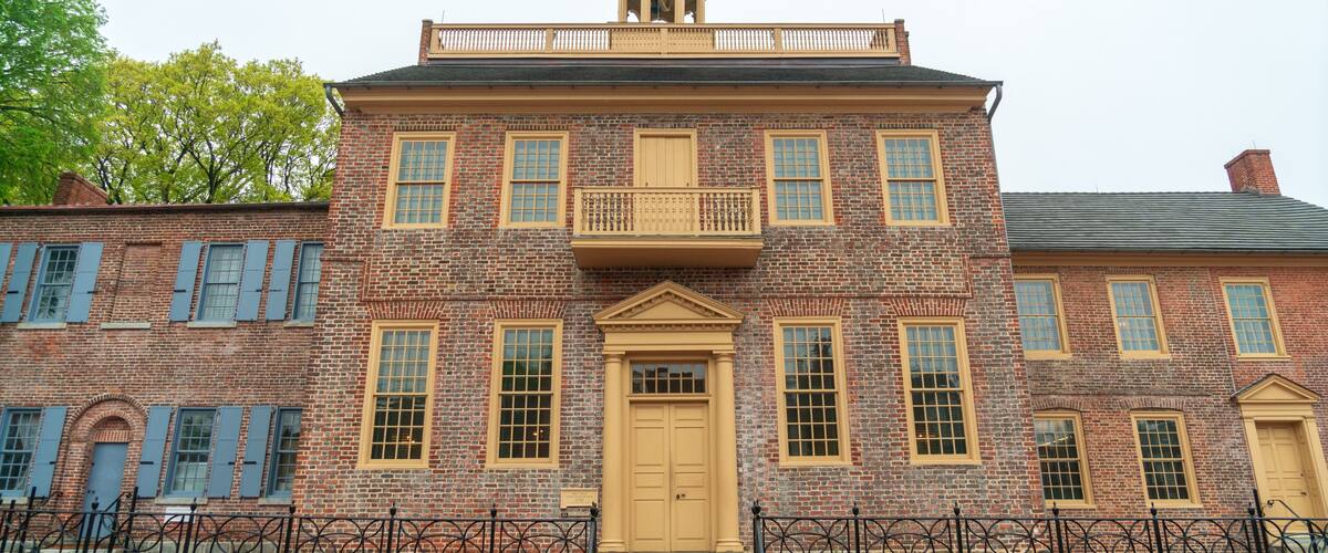 A historic brick building with a central entrance, a balcony, and a small dome on top.