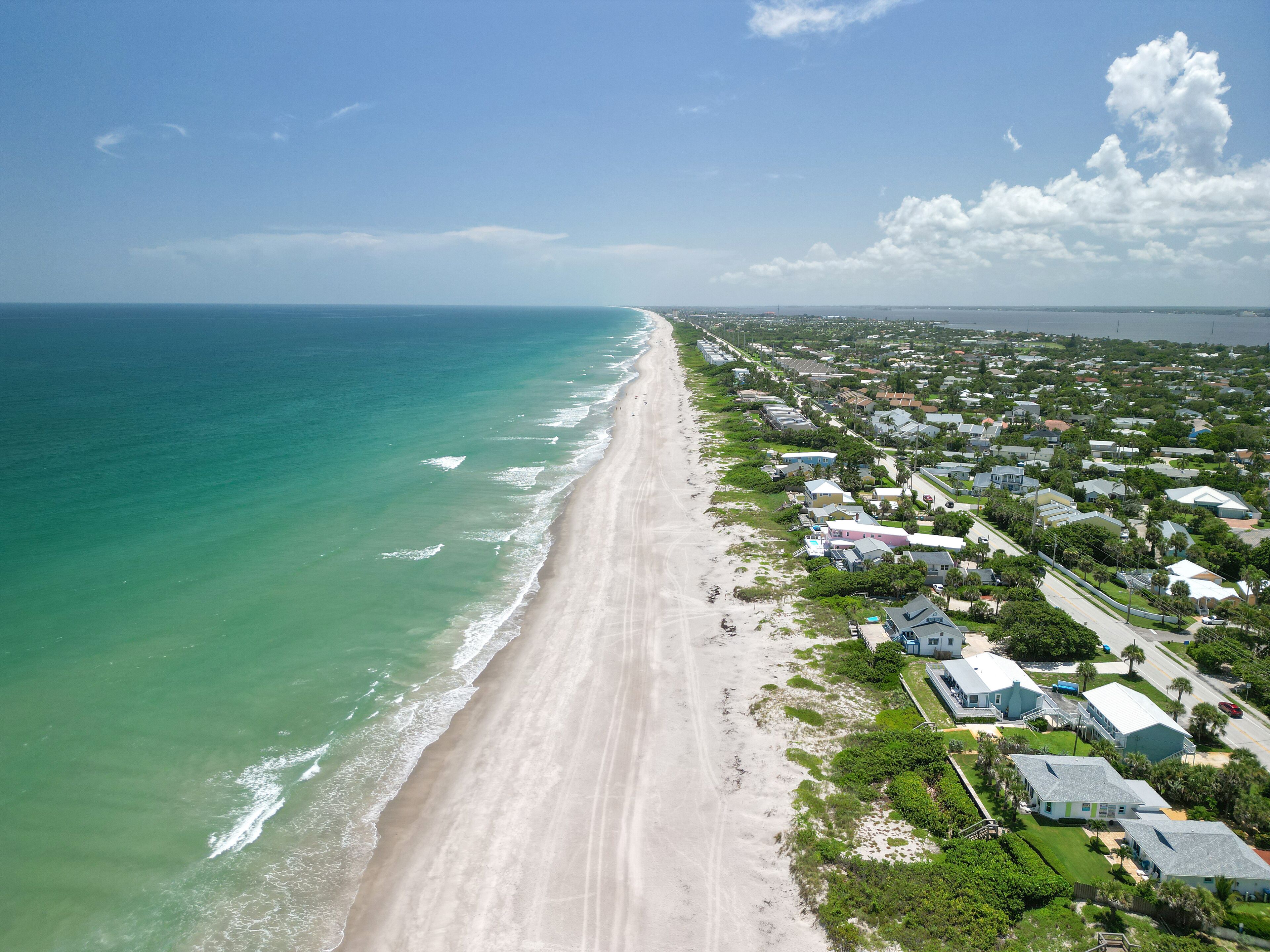 A coastal town with a long sandy beach, houses, and a clear blue sky.