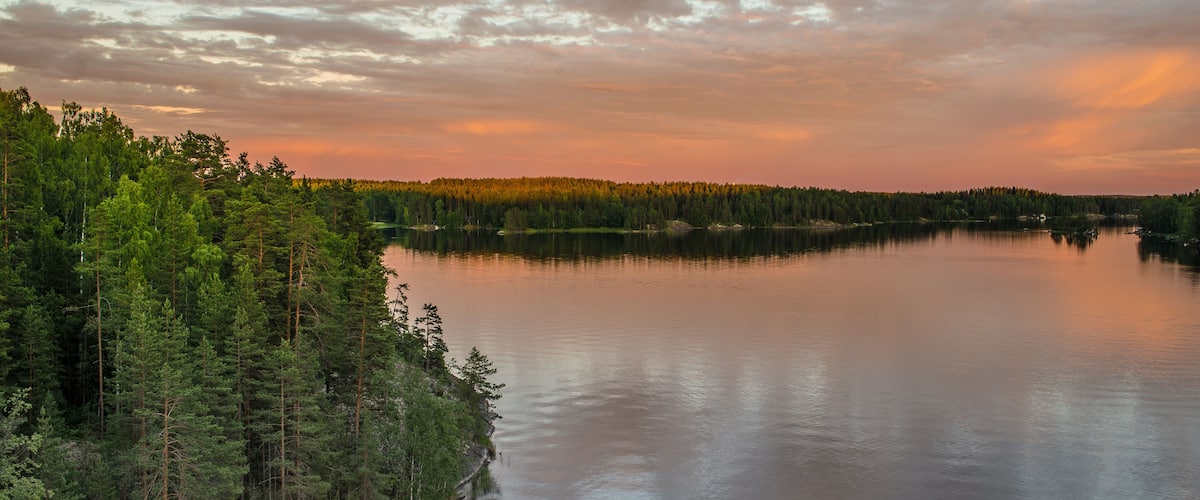 A calm lake surrounded by dense forest and a cloudy sky.