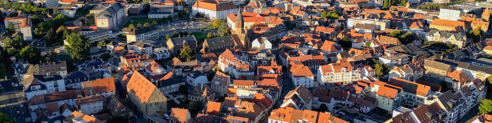 A densely packed town with red-roofed buildings, a prominent church, and a river in the background.
