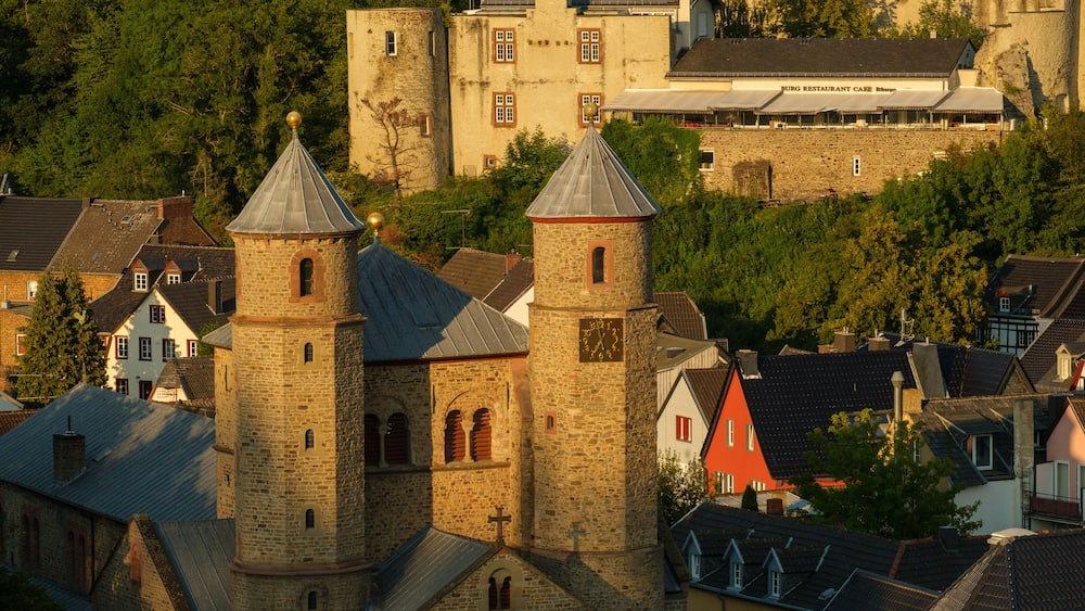 A historic church with two towers, a stone building with a clock, and a restaurant café in the background.