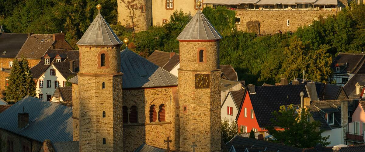 A historic church with two towers, a stone building with a clock, and a restaurant café in the background.