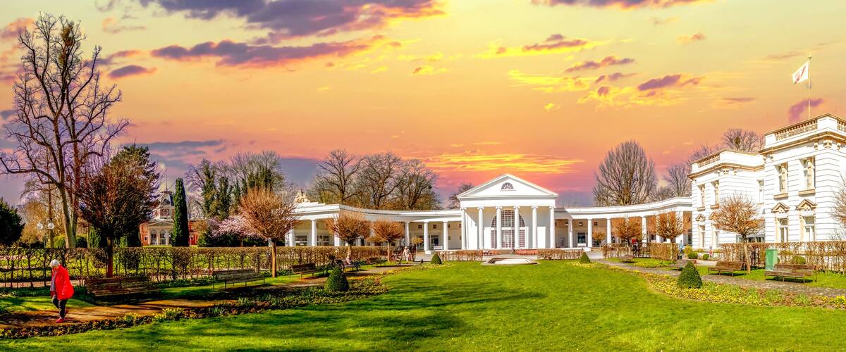 A large white building with columns, surrounded by a well-maintained garden and trees.