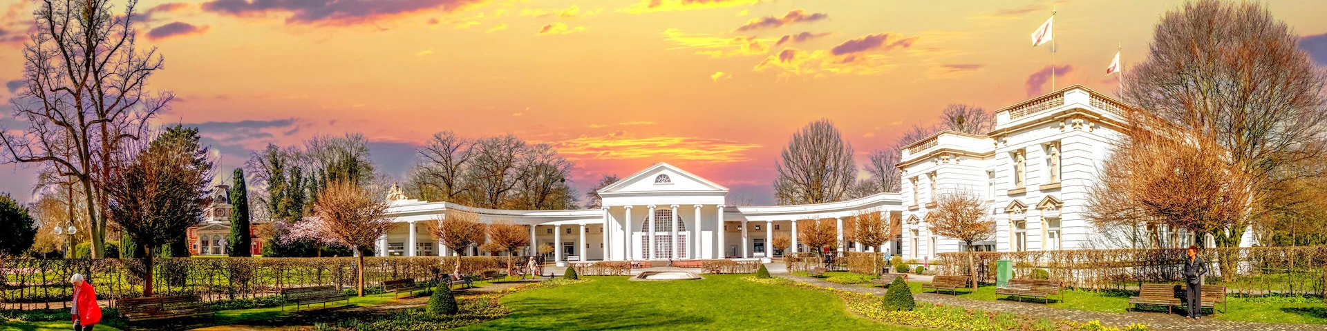 A large white building with columns, surrounded by a well-maintained garden and trees.