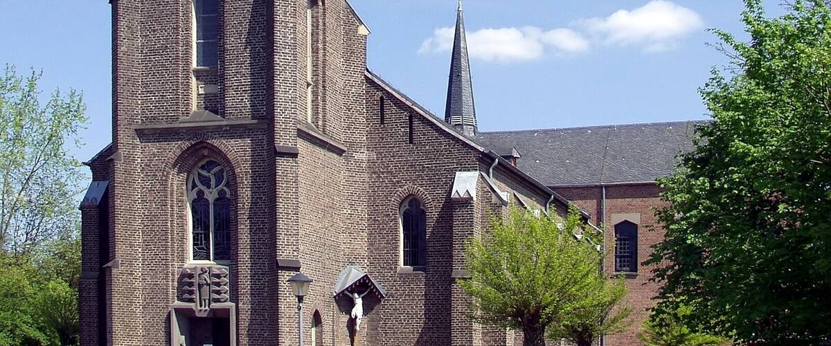 A brick church with a tall steeple and a smaller spire.