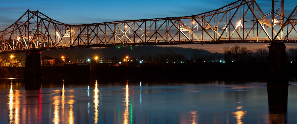 A steel bridge at dusk with lights reflecting on the water.
