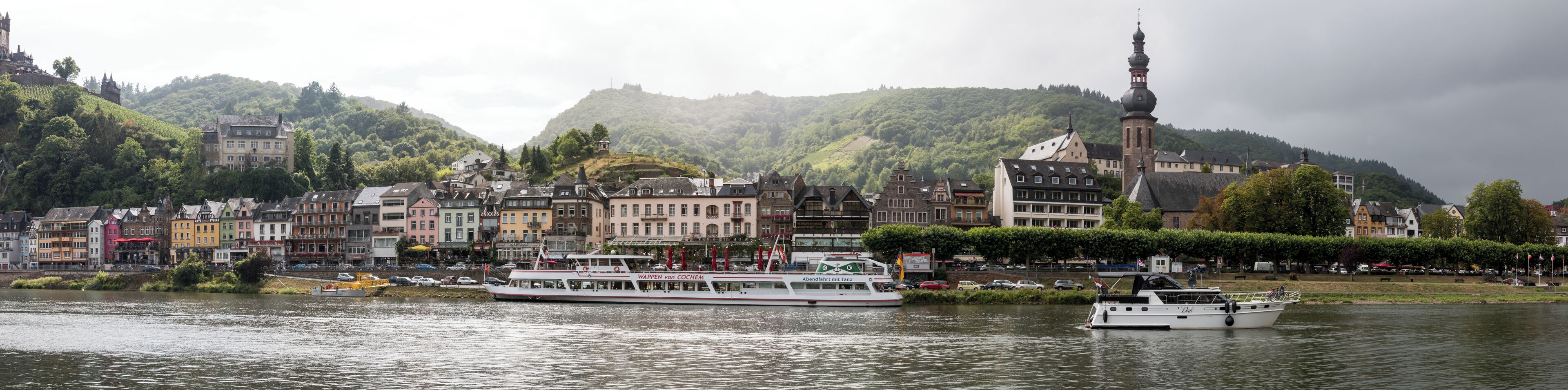 A river with boats, a castle on a hill, and colorful buildings along the riverbank.