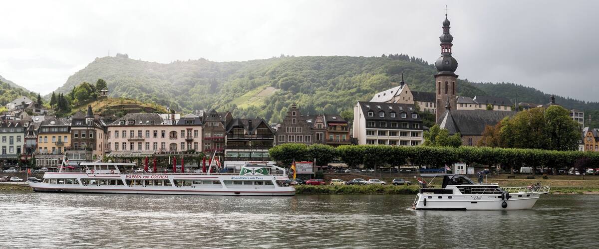A river with boats, a castle on a hill, and colorful buildings along the riverbank.