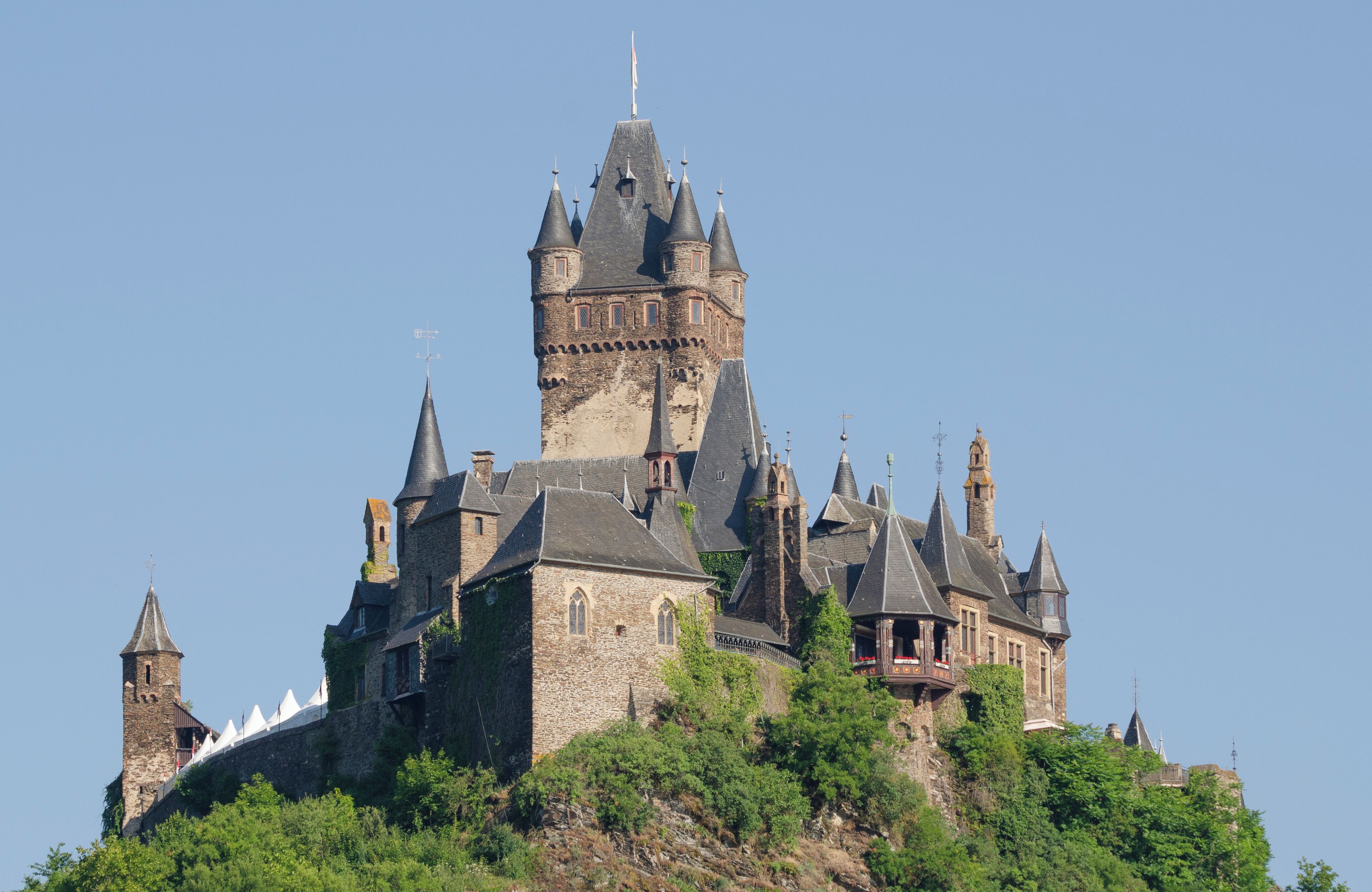 A large, historic castle with multiple towers and turrets, surrounded by lush greenery.