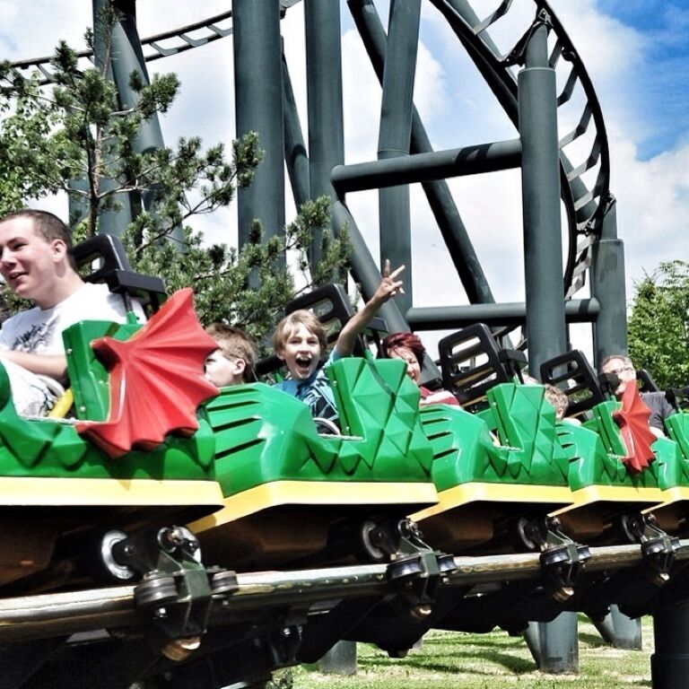 A roller coaster with green cars and red accents, surrounded by trees and a clear sky.