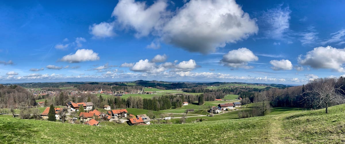 A rural landscape with rolling hills, a village with red-roofed houses, and a church steeple.