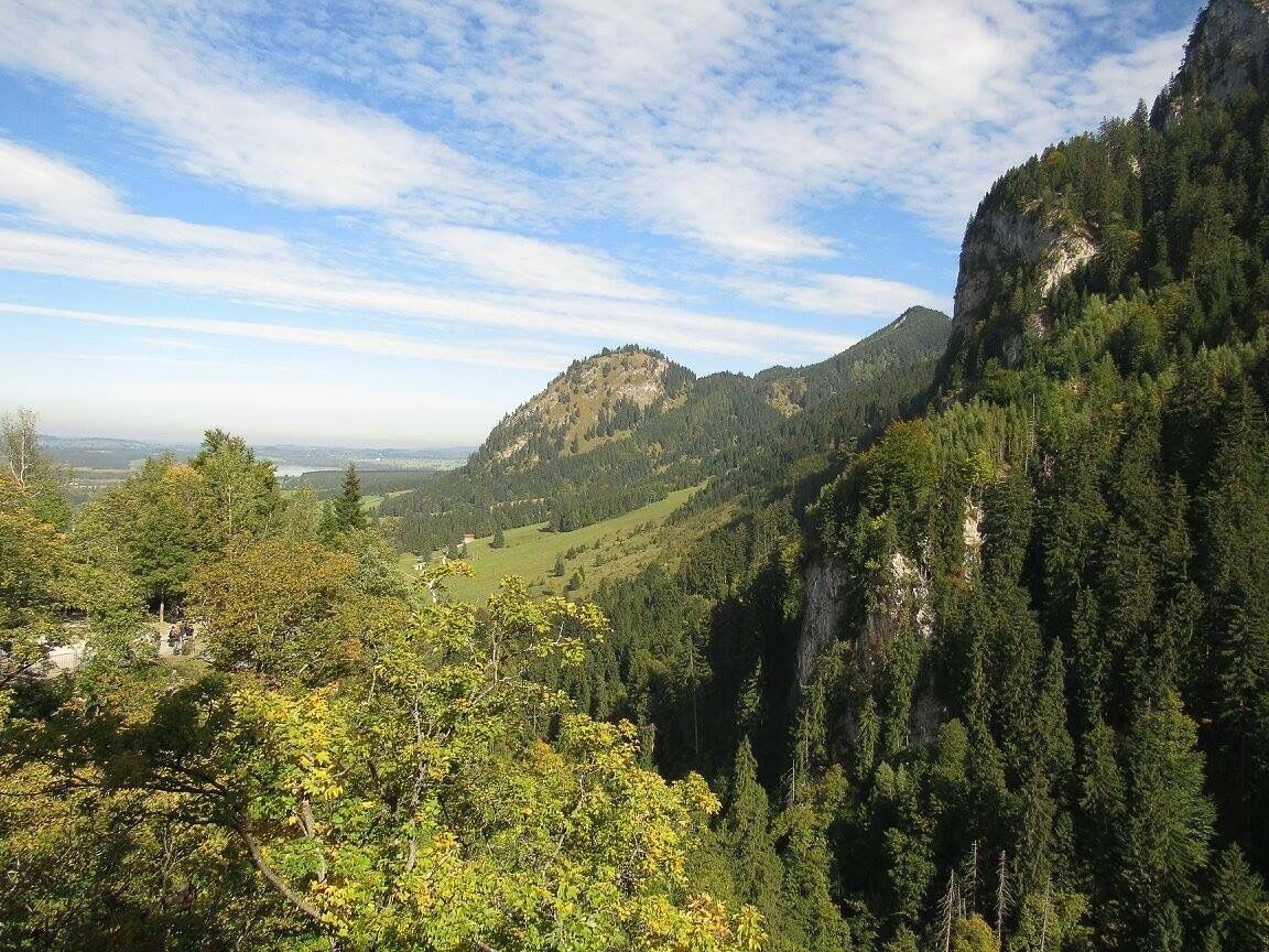 A mountainous landscape with dense forests, a prominent rocky peak, and a distant view of a valley.