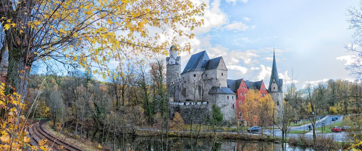 A castle by a river with autumn leaves, reflecting the structure.