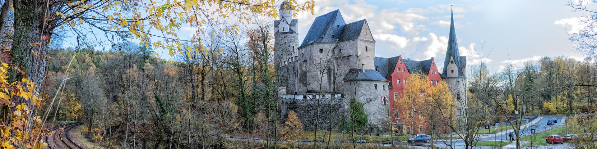 A castle by a river with autumn leaves, reflecting the structure.