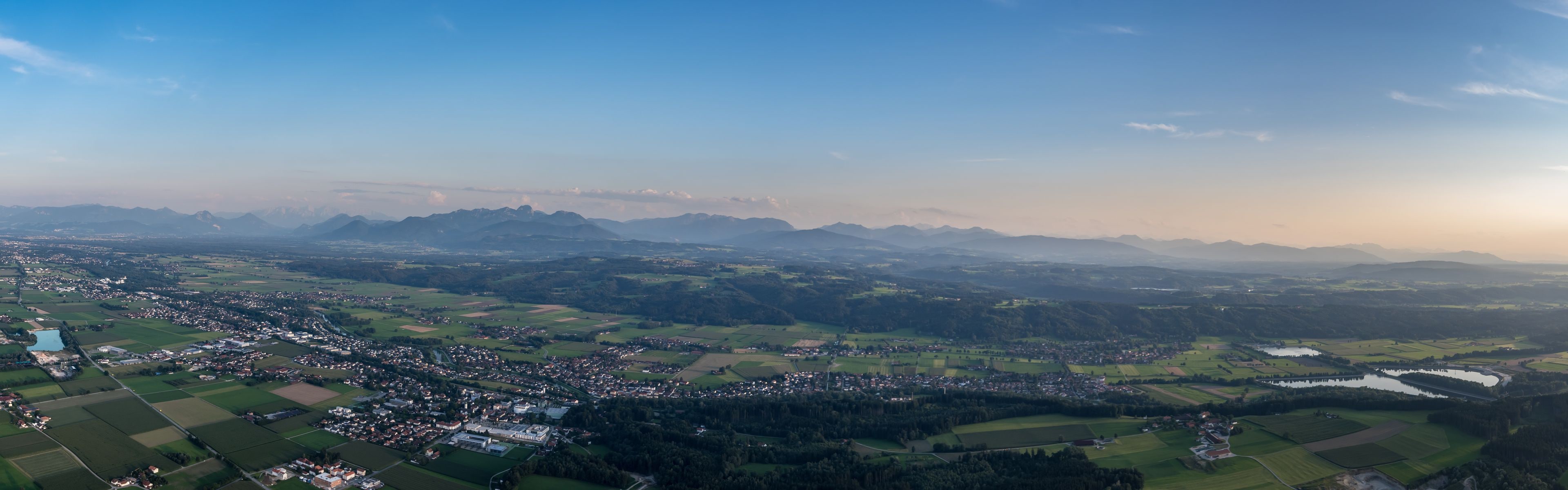 A panoramic view of a town nestled in a valley with surrounding mountains and fields.