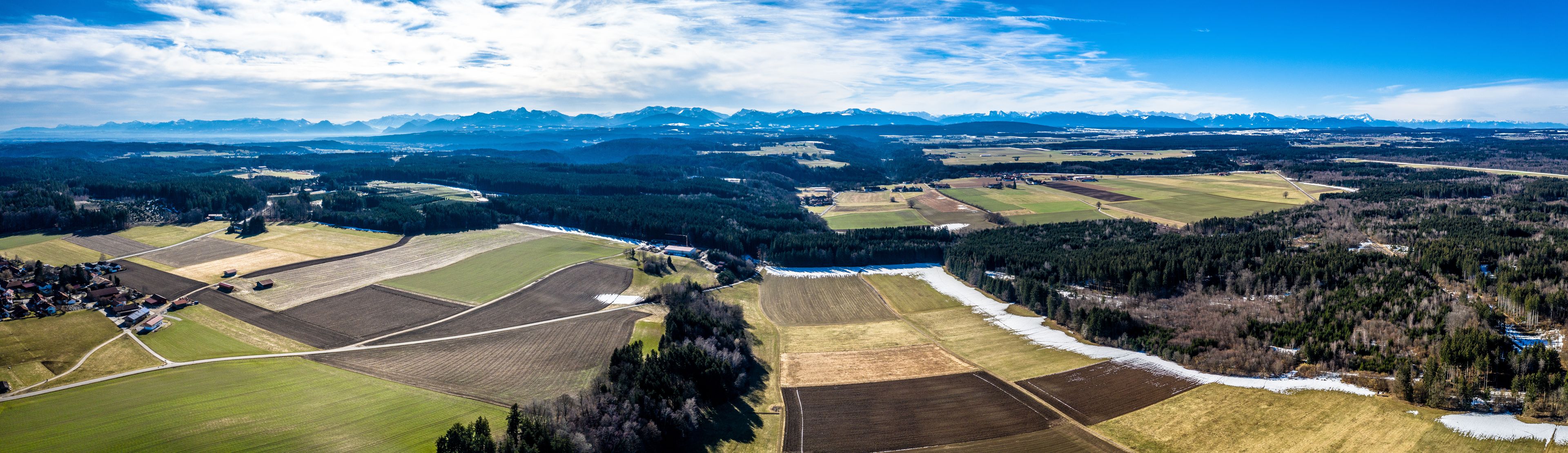 A rural landscape with fields, a river, and distant mountains.