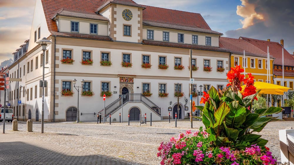 Un bâtiment historique doté d’un clocher, d’un toit recouvert de tuiles rouges et de jardinières fleuries.