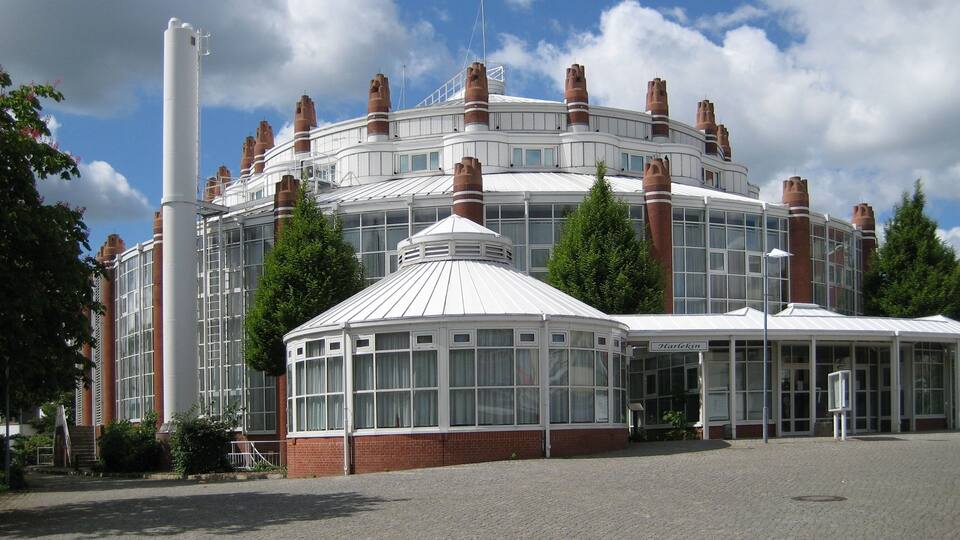 A modern building with a circular design, featuring multiple chimneys and large windows.