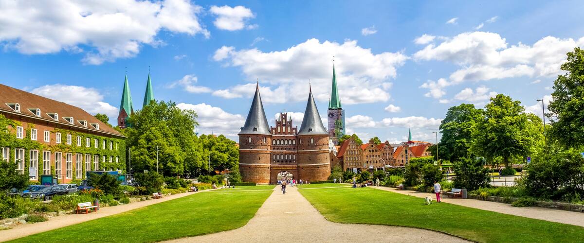 A historic building with three spires, surrounded by lush green lawns and trees.