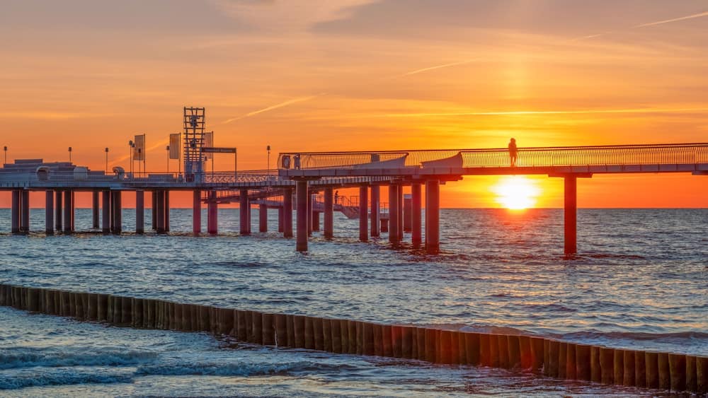 Une jetée qui s’avance dans l’océan au coucher du soleil, le soleil disparaissant à l’horizon.