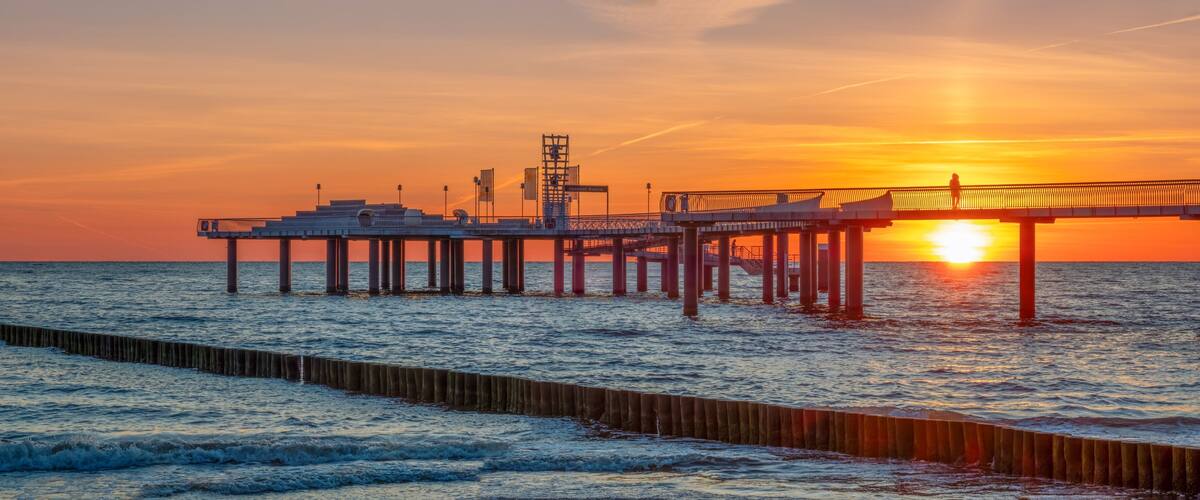 A pier extending into the ocean at sunset with the sun setting on the horizon.