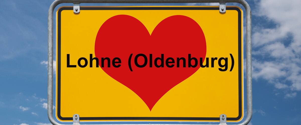 A yellow sign with a red heart and the text "Lohne (Oldenburg)" against a blue sky with clouds.