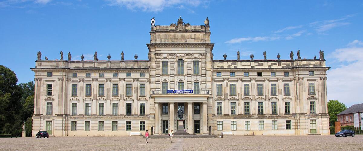 A historic building with statues on the roof, large windows, and a paved courtyard.