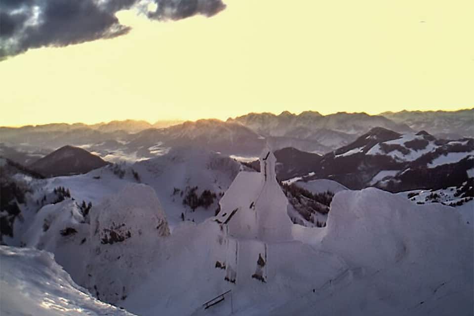 A snow-covered mountain landscape with a prominent peak and a church-like structure in the foreground.