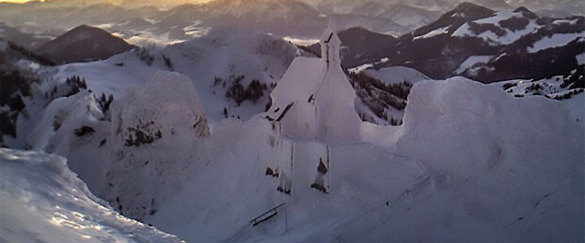 A snow-covered mountain landscape with a prominent peak and a church-like structure in the foreground.