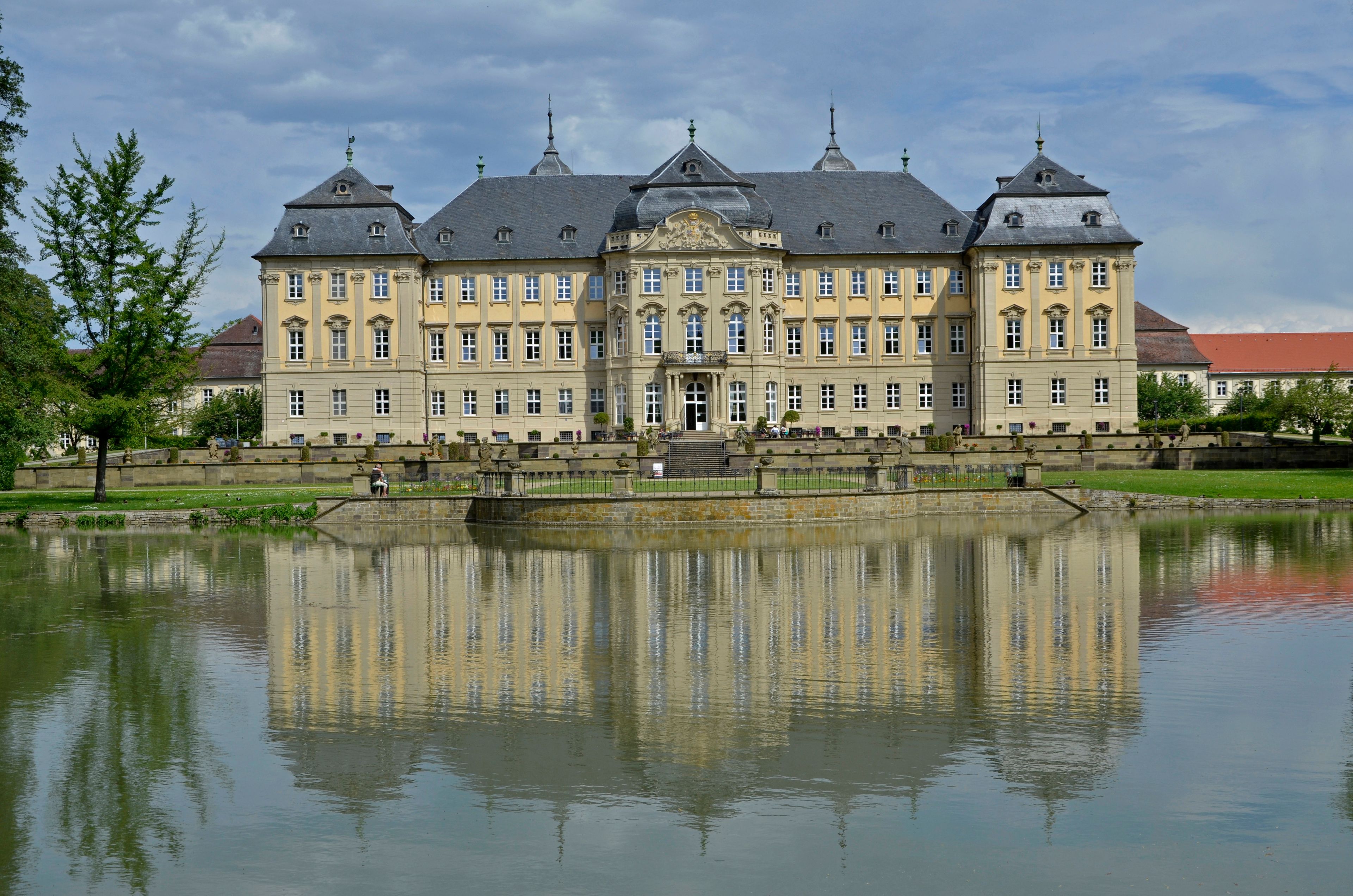 A large, ornate building with multiple towers and a reflective pond in front.