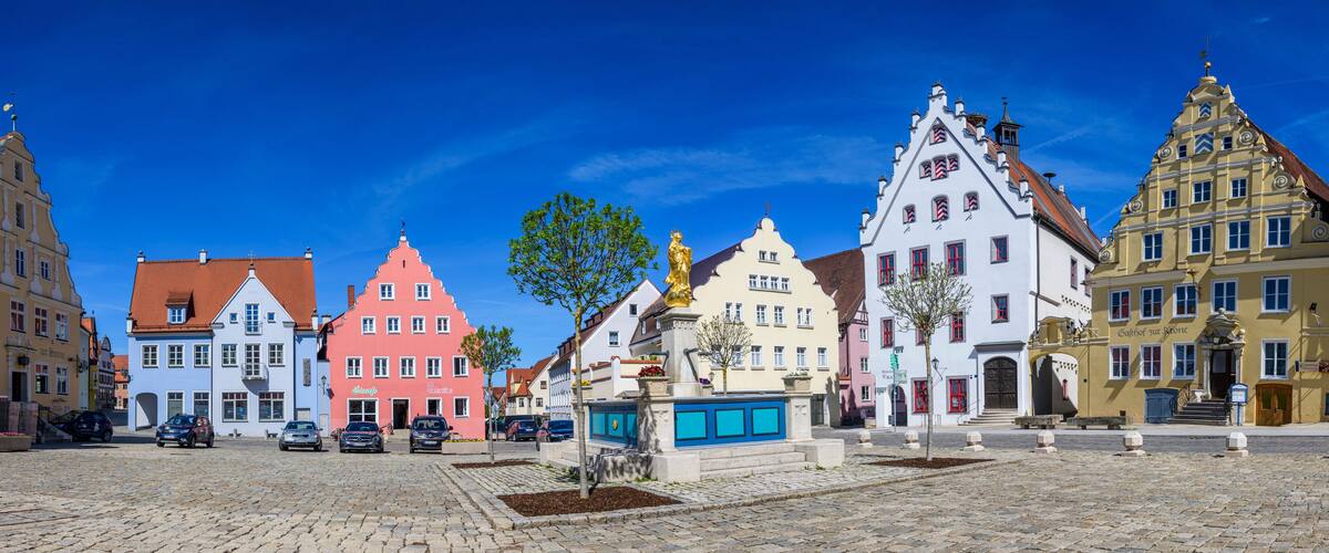 A cobblestone square with colorful historic buildings, a statue, and a fountain.
