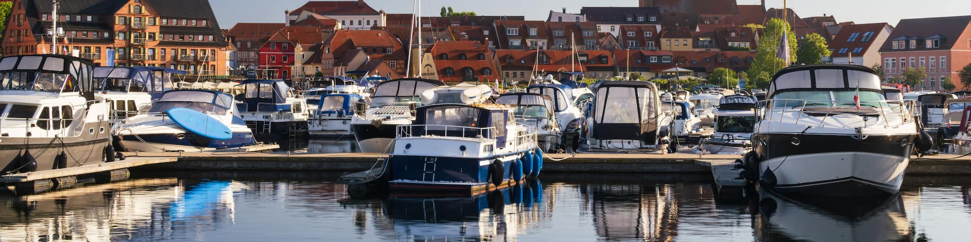 A marina with various boats docked, a clear sky, and historic buildings in the background.