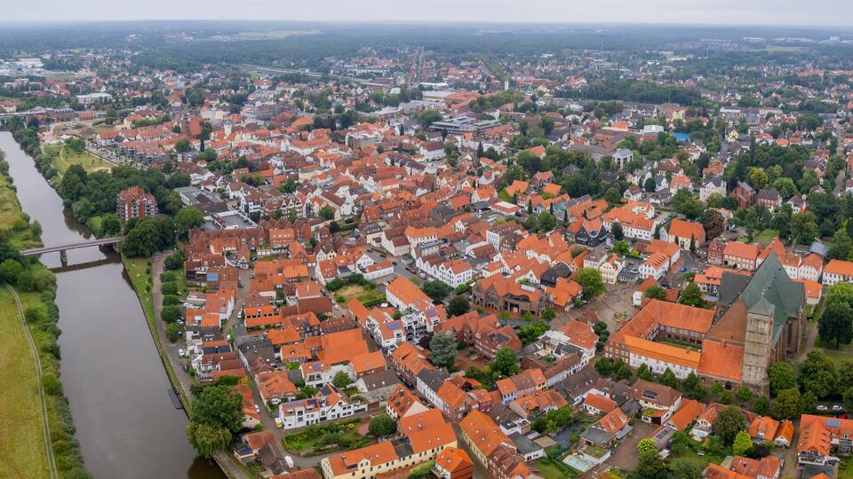 An aerial view of a town with red-roofed buildings, a river, and a bridge.