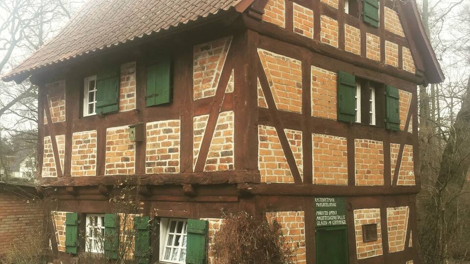 A traditional half-timbered house with a steeply pitched roof, green shutters, and a brick facade.