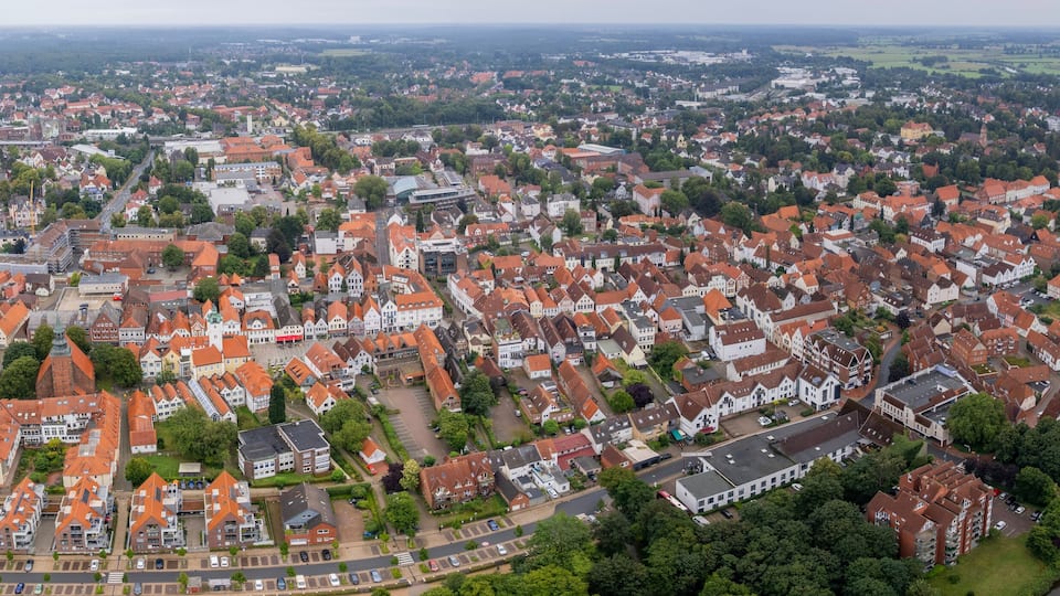 An aerial view of a town with red-roofed buildings, a river, and a bridge.