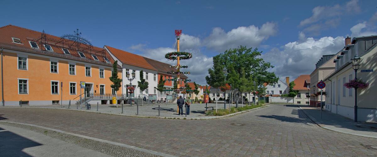 A cobblestone street with historic buildings, a fountain, and a clear blue sky.