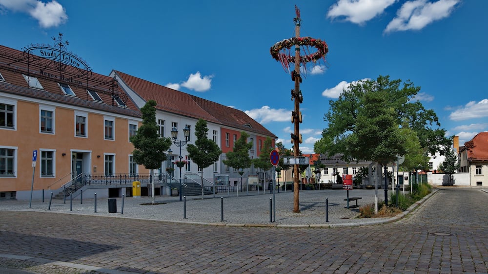 Ein Kopfsteinpflasterplatz mit historischen Gebäuden, einer Ziergalerie und blauem Himmel.