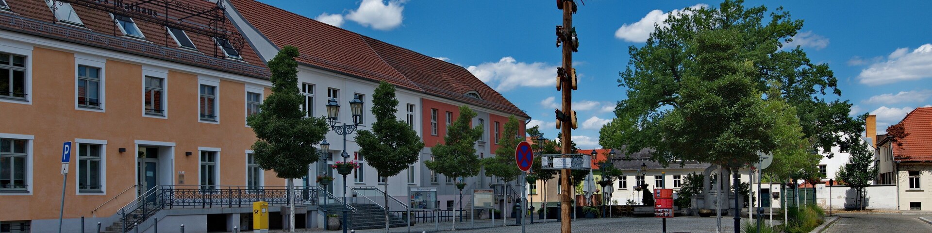 Ein Kopfsteinpflasterplatz mit historischen Gebäuden, einer Ziergalerie und blauem Himmel.