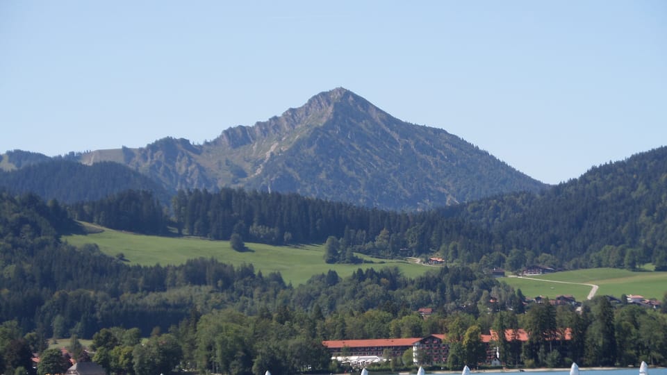 A lake with sailboats, surrounded by green hills and a mountain in the background.